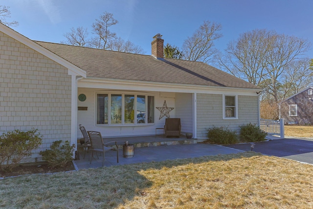 exterior space featuring a front yard, roof with shingles, a chimney, and a patio area