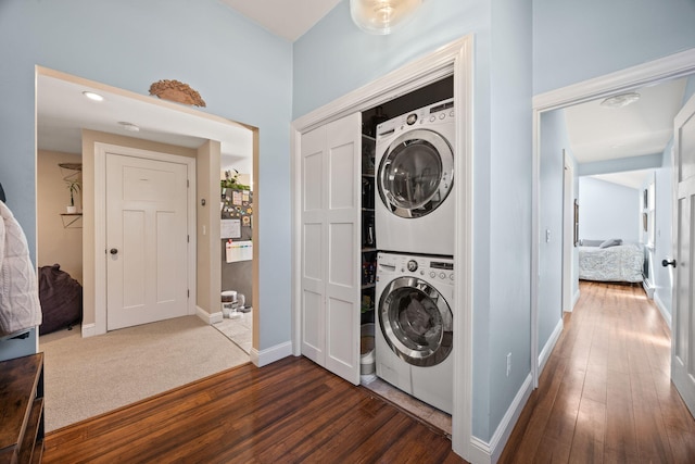 clothes washing area featuring baseboards, stacked washer and clothes dryer, dark wood finished floors, and laundry area