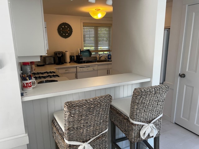 kitchen featuring white cabinets, a kitchen breakfast bar, white dishwasher, and sink