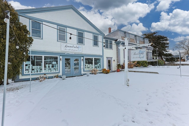 snow covered rear of property with french doors and a chimney