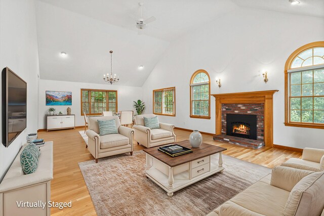 living room featuring ceiling fan with notable chandelier, high vaulted ceiling, a brick fireplace, and light hardwood / wood-style floors