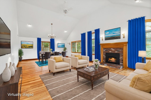 living room with hardwood / wood-style flooring, ceiling fan with notable chandelier, high vaulted ceiling, and a fireplace