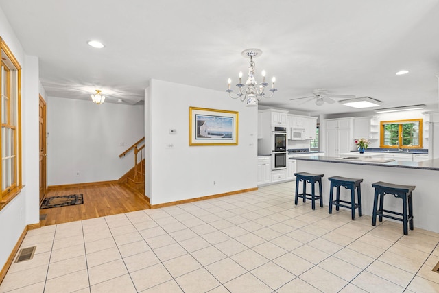 kitchen with stainless steel double oven, a kitchen bar, white cabinetry, kitchen peninsula, and light tile patterned floors