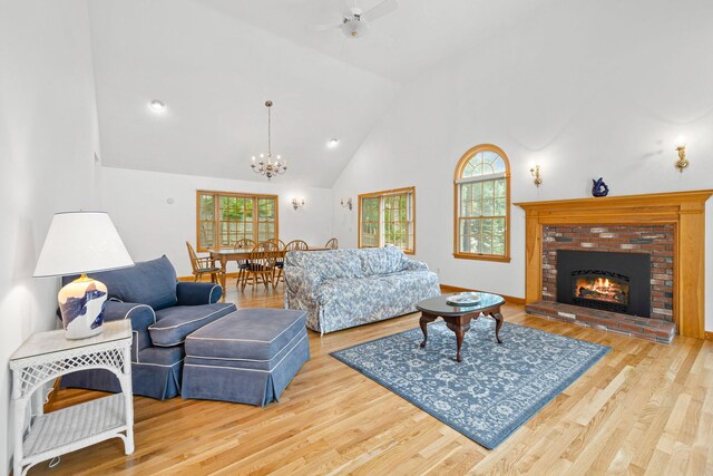 living room featuring light wood-type flooring, ceiling fan with notable chandelier, high vaulted ceiling, and a fireplace