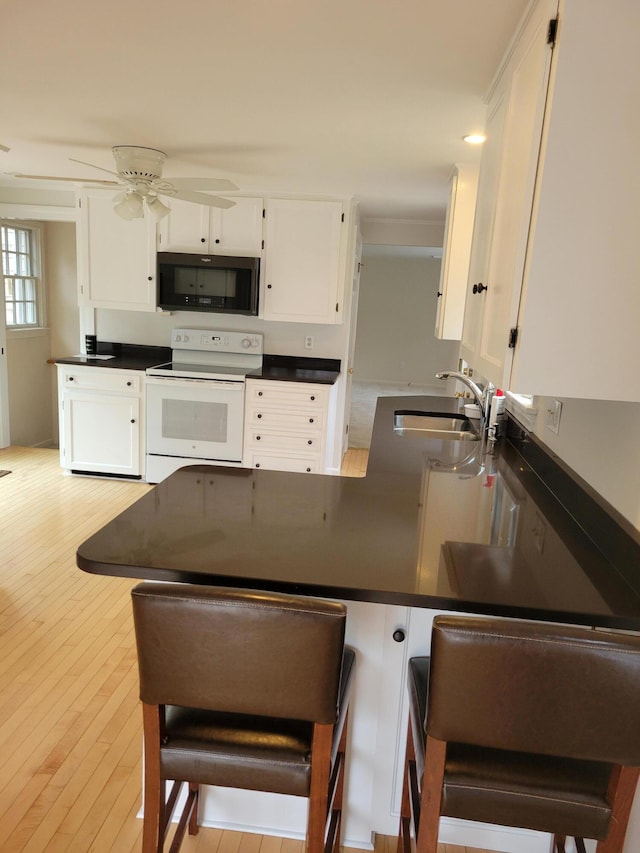 kitchen with a sink, white cabinetry, white range with electric stovetop, a peninsula, and black microwave