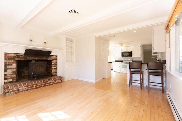 living area featuring visible vents, beam ceiling, light wood finished floors, a baseboard radiator, and a wood stove