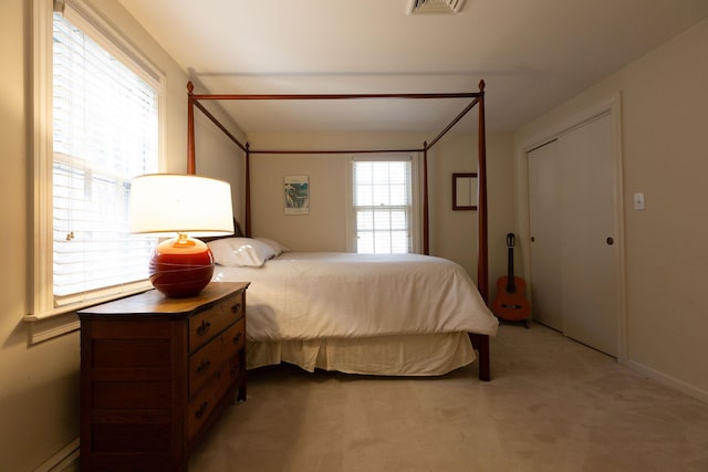 bedroom with a baseboard heating unit, light colored carpet, and visible vents