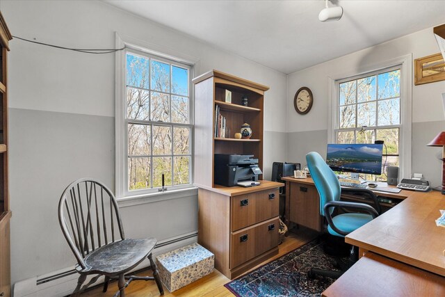 home office featuring wood finished floors, plenty of natural light, and a baseboard heating unit
