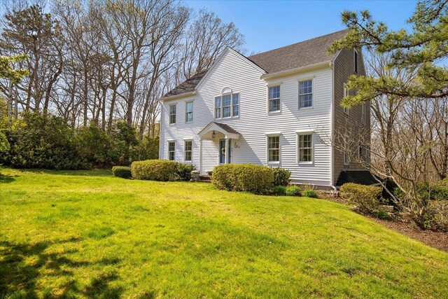 colonial-style house with a front yard and roof with shingles