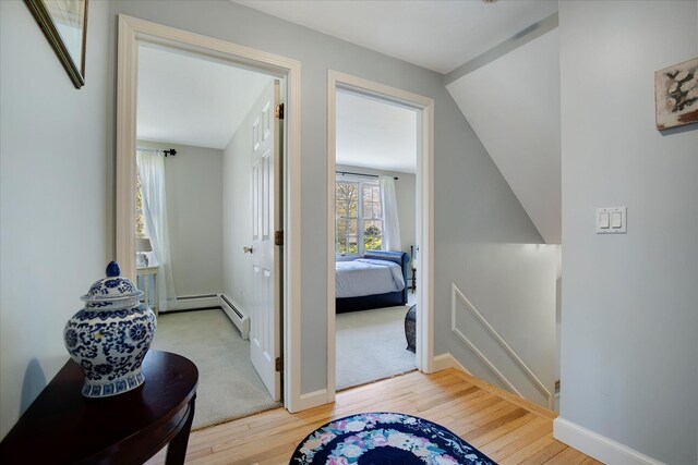 hallway with an upstairs landing, light wood-style floors, baseboard heating, and baseboards