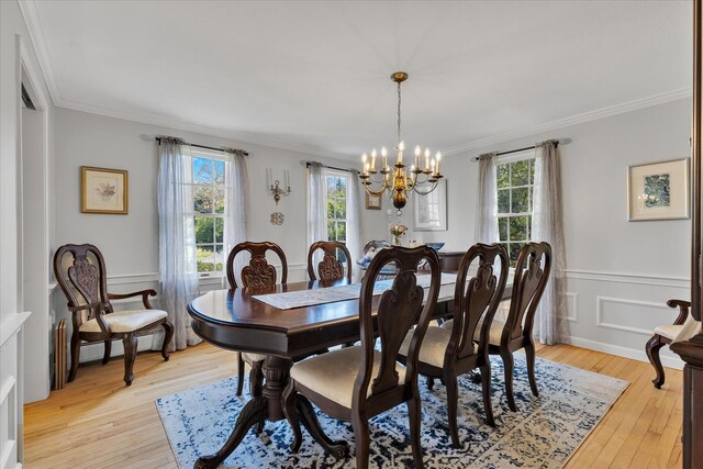 dining space with plenty of natural light, crown molding, a chandelier, light wood-type flooring, and a wainscoted wall