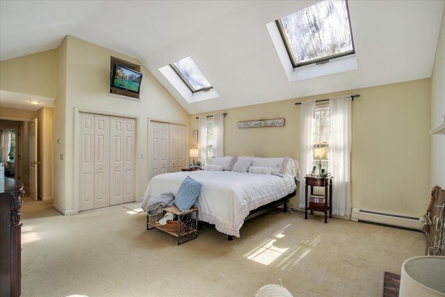 bedroom featuring a skylight, baseboard heating, two closets, carpet, and high vaulted ceiling