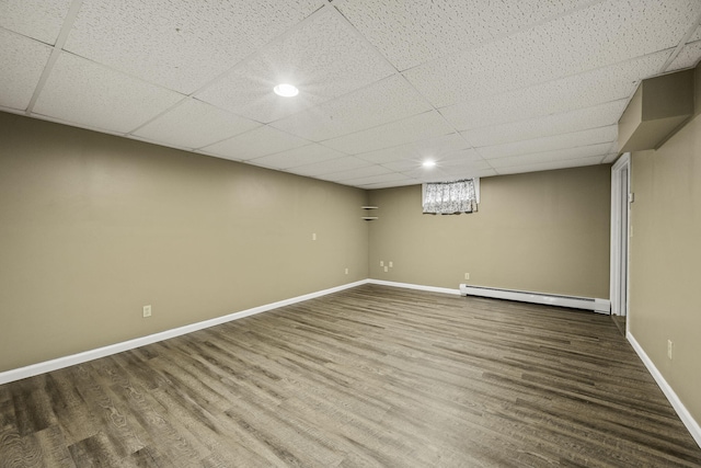 basement featuring wood-type flooring, a baseboard heating unit, and a drop ceiling