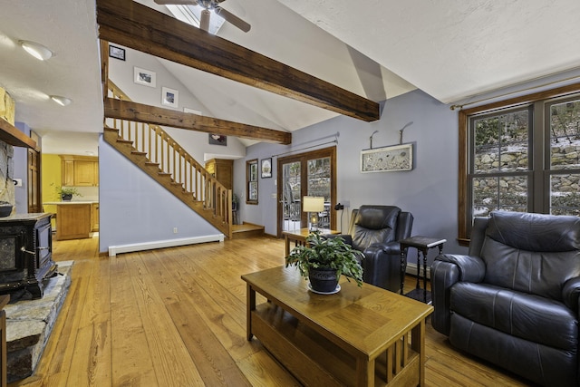 living room featuring lofted ceiling with beams, a wood stove, a baseboard heating unit, ceiling fan, and light wood-type flooring