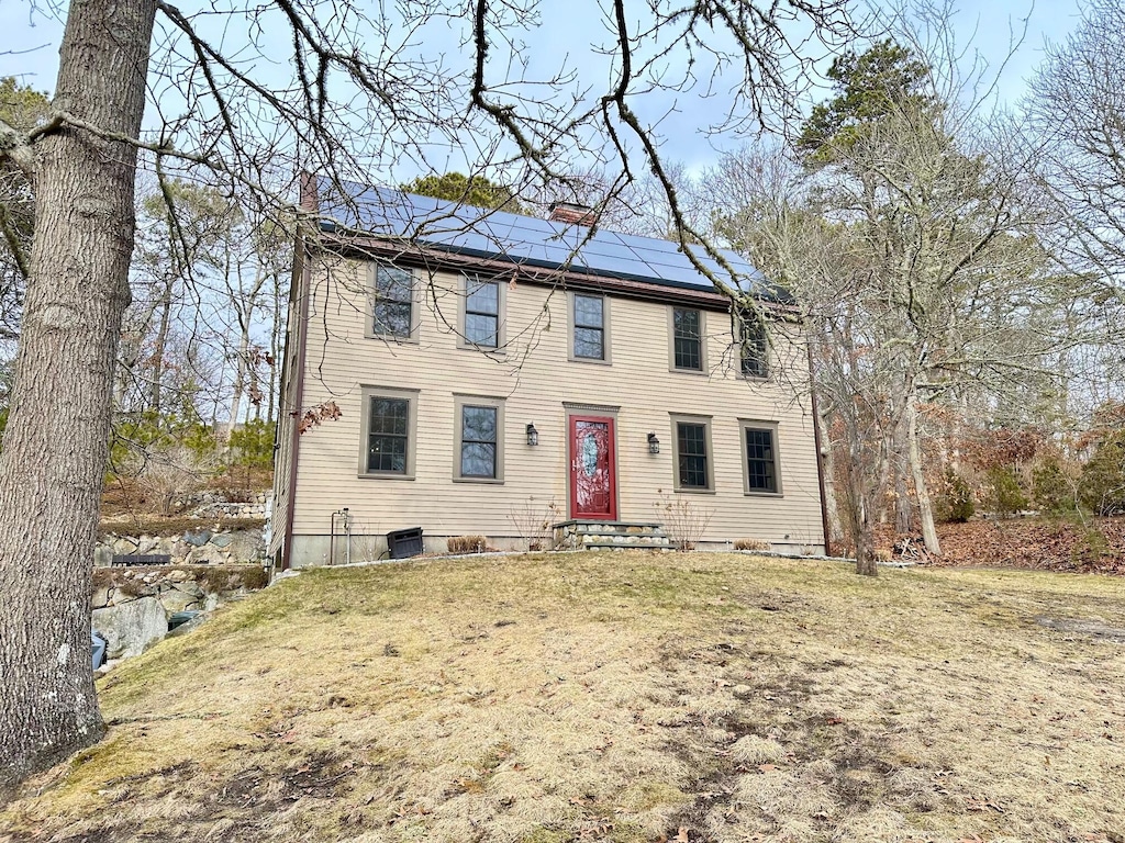 colonial home with central AC unit, entry steps, a chimney, a front yard, and solar panels