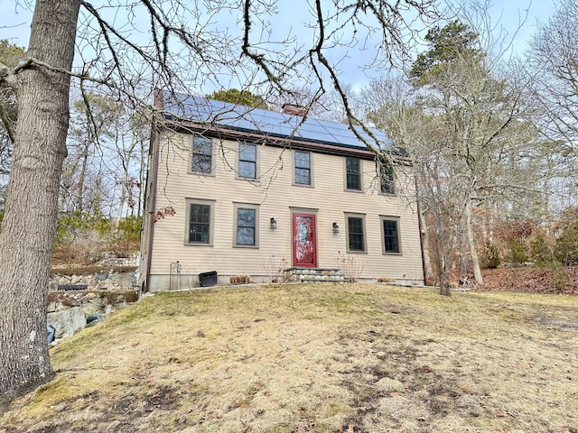 colonial home with central AC unit, entry steps, a chimney, a front yard, and solar panels