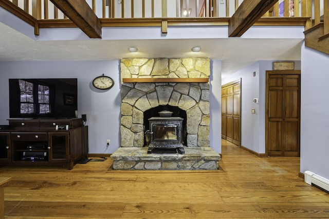 living room featuring a towering ceiling, wood-type flooring, a wood stove, and baseboard heating