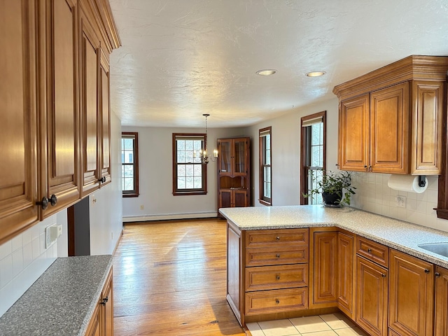 kitchen with a baseboard heating unit, backsplash, light hardwood / wood-style floors, decorative light fixtures, and kitchen peninsula