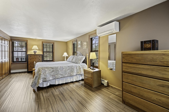 bedroom with baseboard heating, a wall mounted air conditioner, and light hardwood / wood-style flooring