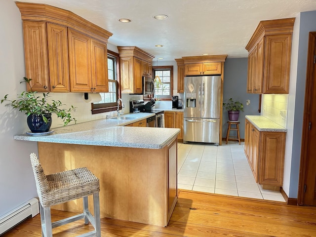 kitchen featuring sink, a breakfast bar area, appliances with stainless steel finishes, kitchen peninsula, and a baseboard heating unit