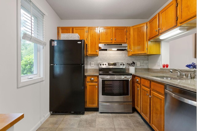 288 Fletcher Ln, Brewster, MA 02631 - kitchen with appliances with stainless steel finishes, under cabinet range hood, decorative backsplash, brown cabinetry, and light stone countertops