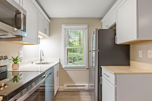 1029 Iyannough Rd Unit 9B, Hyannis, MA 02601 - kitchen with appliances with stainless steel finishes, a baseboard radiator, a sink, wood finished floors, and white cabinets