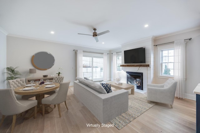 living area with plenty of natural light, light wood-style flooring, a fireplace, and crown molding