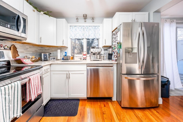 kitchen featuring white cabinetry, decorative backsplash, sink, light hardwood / wood-style flooring, and stainless steel appliances