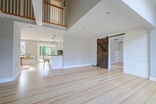 unfurnished living room with a towering ceiling, light hardwood / wood-style floors, and a barn door