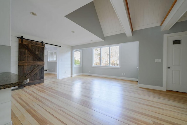 unfurnished living room featuring a barn door, light hardwood / wood-style floors, and beam ceiling