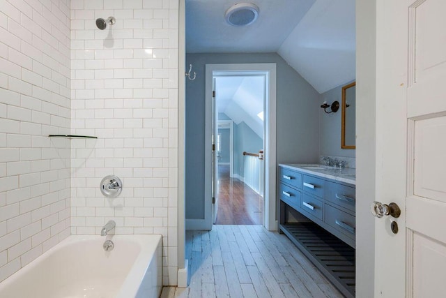 bathroom with tiled shower / bath combo, vanity, vaulted ceiling, and wood-type flooring