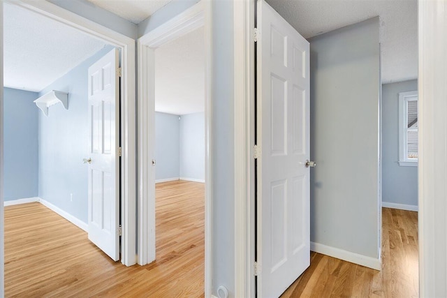 hall with light wood-type flooring and a textured ceiling