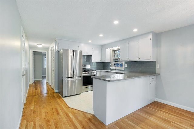 kitchen featuring white cabinets, appliances with stainless steel finishes, decorative backsplash, kitchen peninsula, and light wood-type flooring