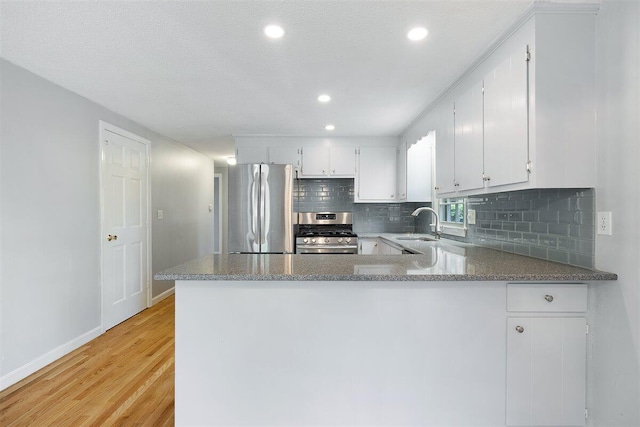 kitchen with kitchen peninsula, white cabinets, light hardwood / wood-style flooring, and stainless steel appliances