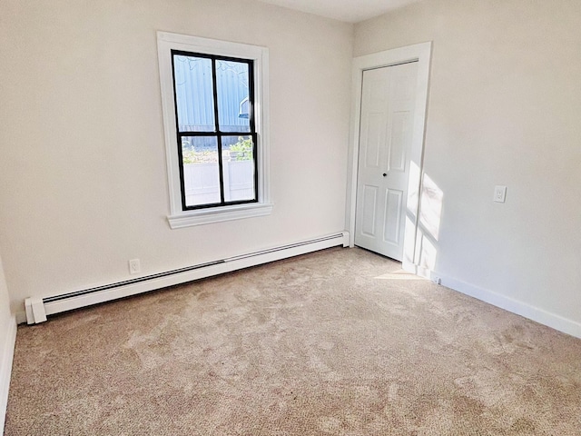 carpeted spare room featuring a baseboard heating unit and baseboards