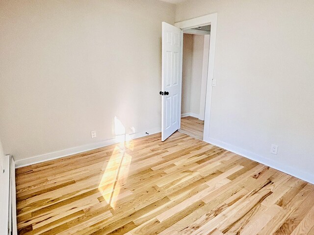 empty room with light wood finished floors, baseboards, and a baseboard heating unit