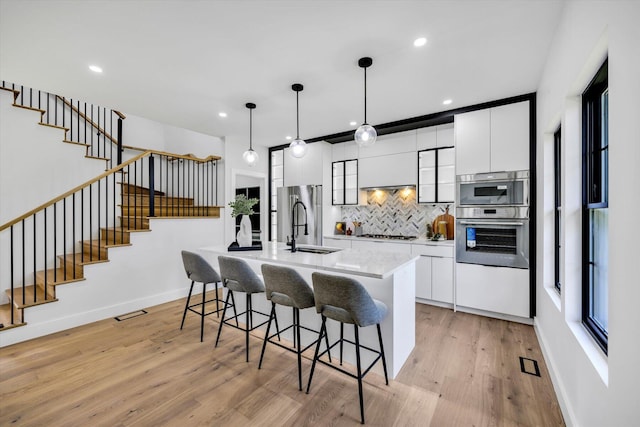 2 Buttercup Ln, South Yarmouth, MA 02664 - kitchen with appliances with stainless steel finishes, backsplash, a breakfast bar, light wood finished floors, and a kitchen island with sink