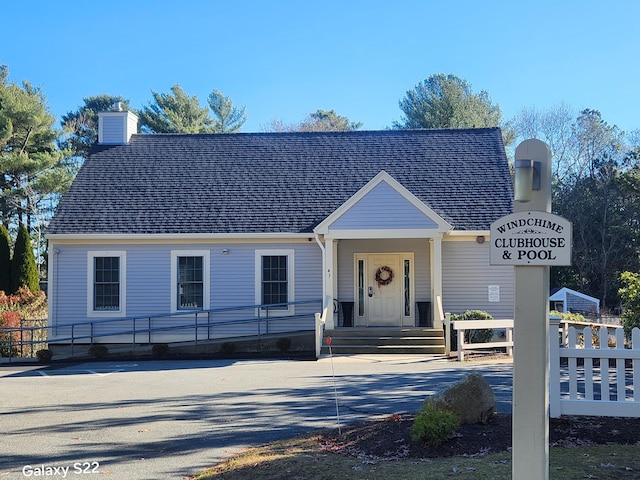 view of front of home with a shingled roof, fence, and a chimney