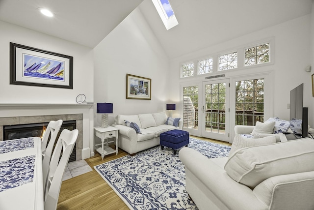 living area with recessed lighting, a tile fireplace, a skylight, wood finished floors, and high vaulted ceiling