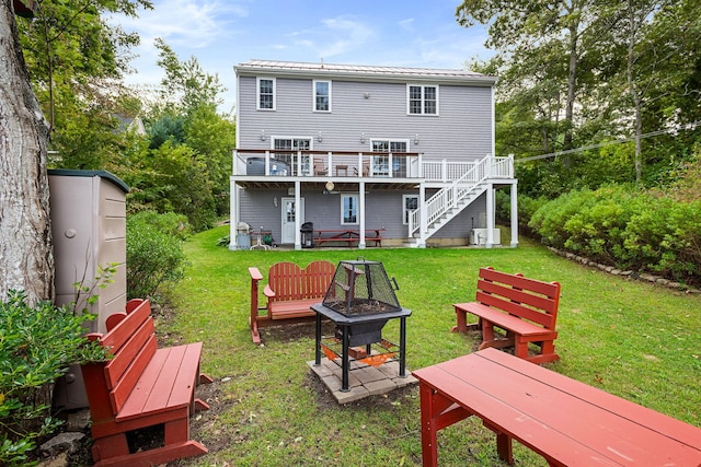 rear view of house with a fire pit, a wooden deck, stairs, and a lawn