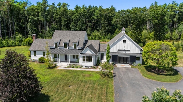 view of front facade featuring asphalt driveway, a standing seam roof, board and batten siding, a front yard, and a porch