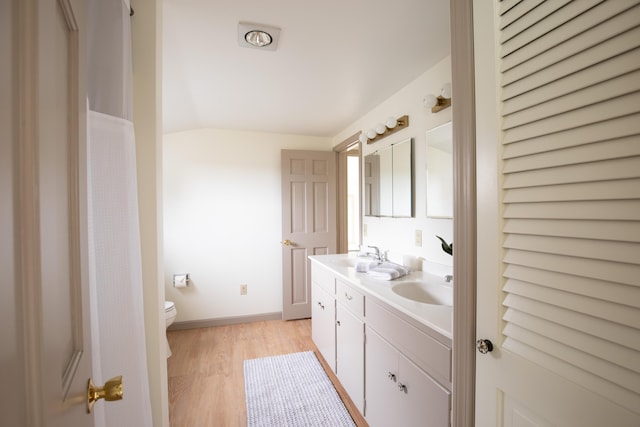 bathroom featuring wood-type flooring, lofted ceiling, vanity, and toilet