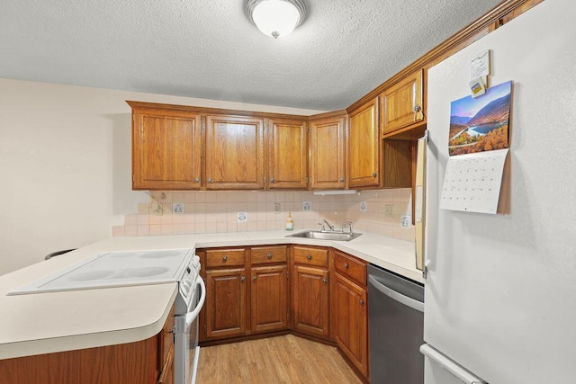 kitchen with sink, light wood-type flooring, tasteful backsplash, white appliances, and a textured ceiling