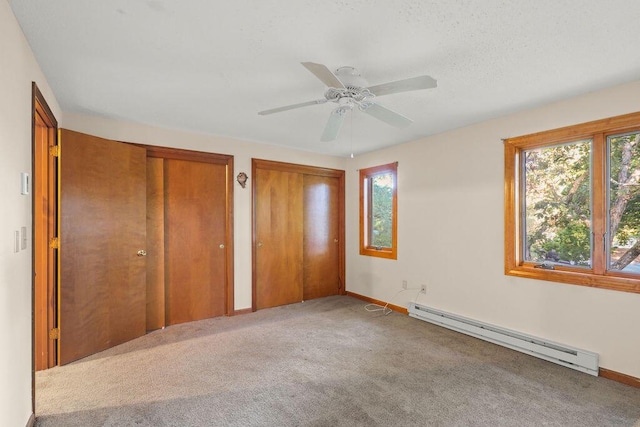 unfurnished bedroom featuring baseboard heating, carpet floors, two closets, and ceiling fan