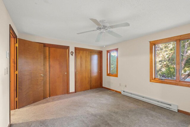 unfurnished bedroom featuring baseboard heating, carpet floors, two closets, and ceiling fan