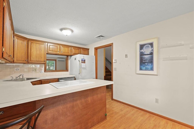 kitchen featuring a textured ceiling, white fridge, sink, kitchen peninsula, and light hardwood / wood-style flooring