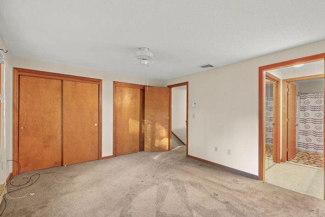 unfurnished bedroom featuring ceiling fan, light colored carpet, and two closets