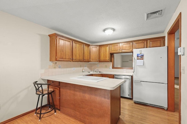 kitchen with white fridge, stainless steel dishwasher, sink, light hardwood / wood-style flooring, and kitchen peninsula