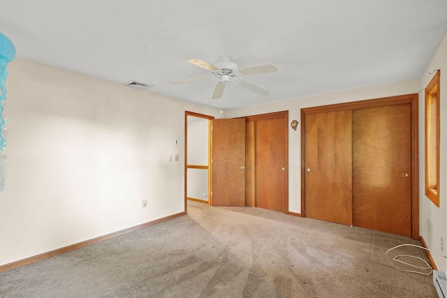 unfurnished bedroom with carpet, baseboard heating, two closets, and ceiling fan