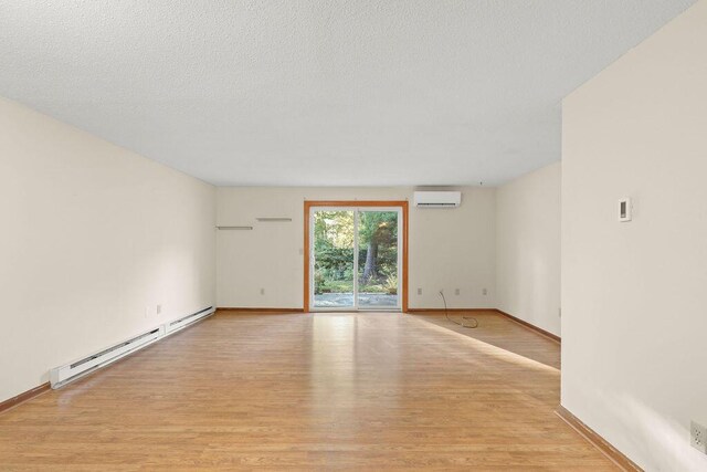 empty room featuring a textured ceiling, a baseboard radiator, a wall mounted AC, and light hardwood / wood-style flooring